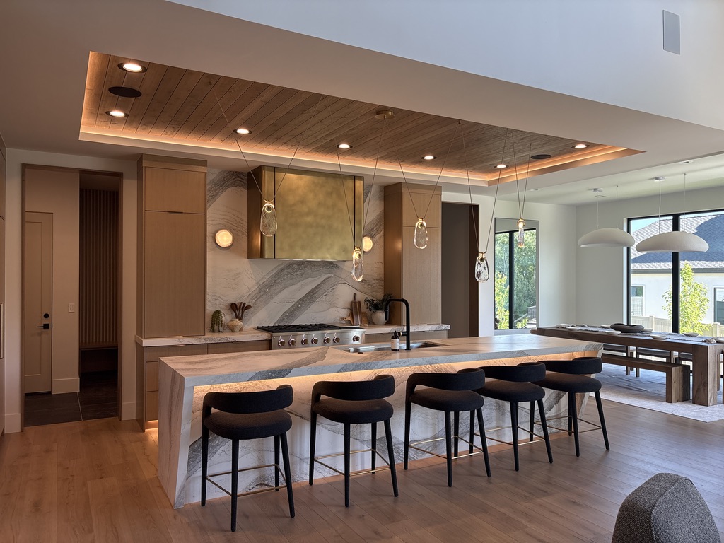 Custom kitchen with wood tray ceiling, backlit marble island, and brass pendant lights