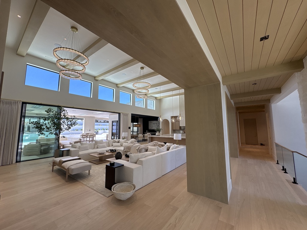 Open concept great room with custom ceiling beams, ring chandeliers, and pool views